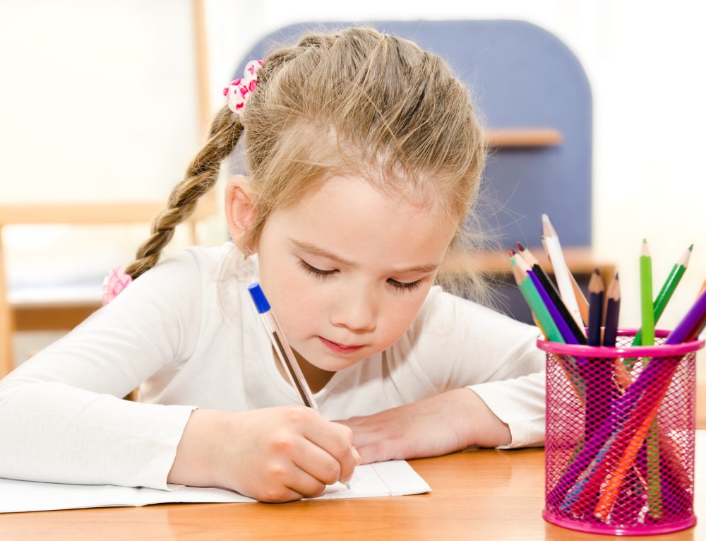 Cute little girl is writing at the desk  in preschool